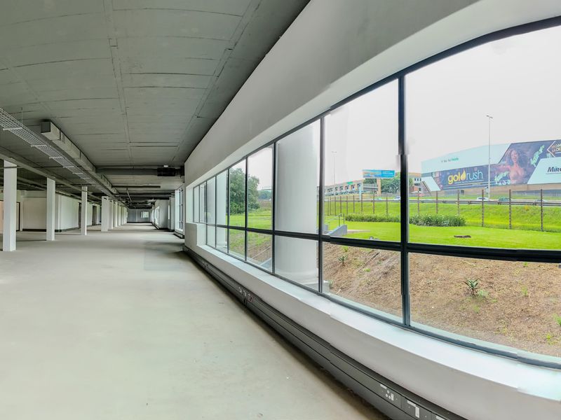 Spacious open-plan industrial interior featuring exposed concrete ceilings, structural columns, and expansive windows providing ample natural light and exterior views.