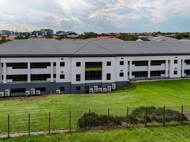 Aerial view of a modern industrial office building featuring a tiled roof, multi-level facade, and external air conditioning units set within a landscaped property.
