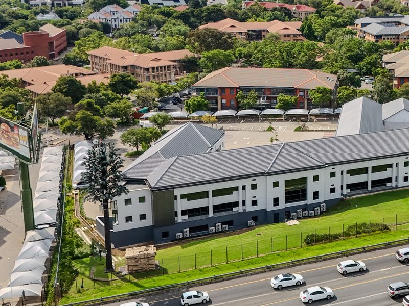 Aerial view of a commercial industrial property featuring a multi-level building, extensive paved parking with shade ports, and well-maintained surrounding grounds.