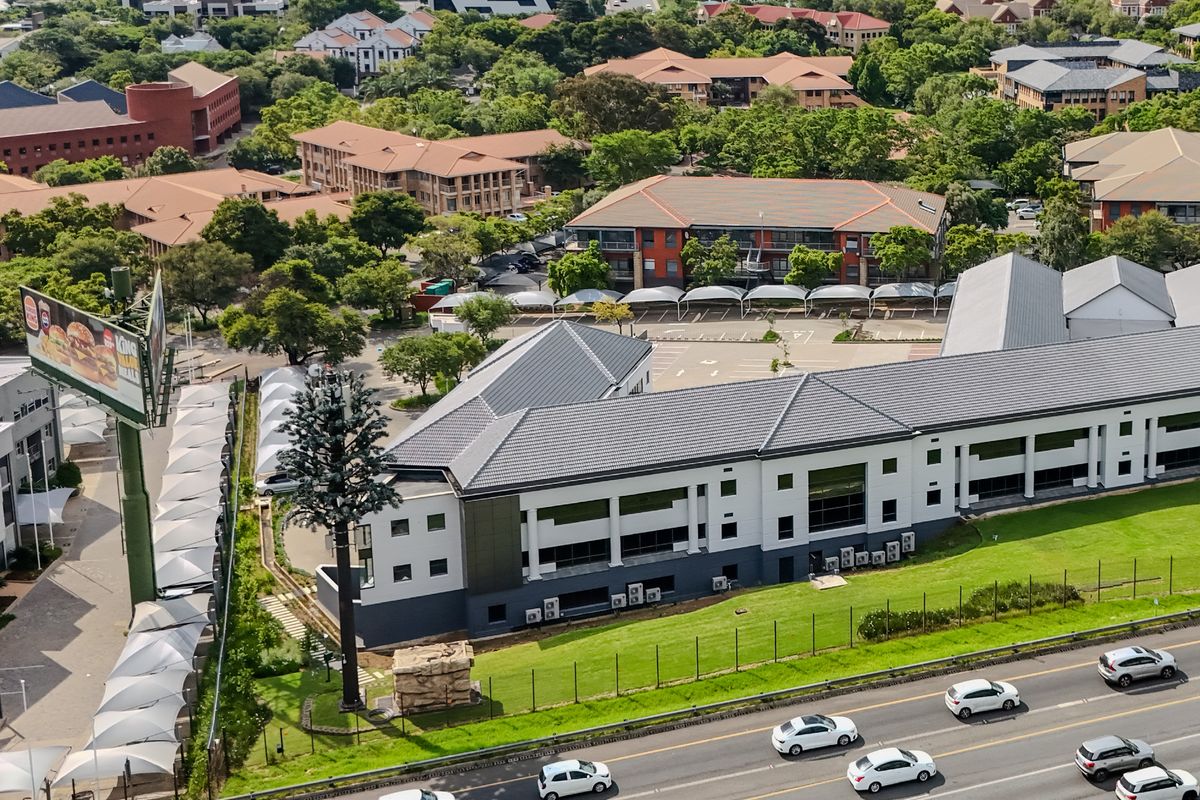 Aerial view of a commercial industrial property featuring a multi-level building, extensive paved parking with shade ports, and well-maintained surrounding grounds.