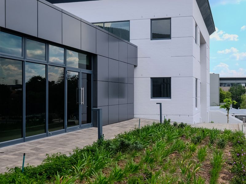 Modern industrial building facade featuring a combination of white painted brickwork and sleek dark grey composite cladding with large glass entrance doors.