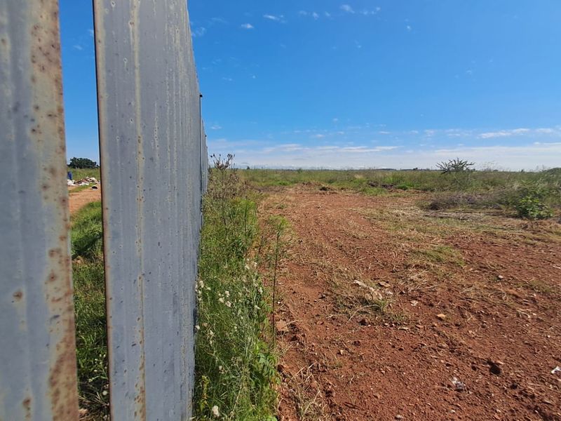 A view of the vacant commercial land featuring a weathered metal perimeter fence and unpaved ground.