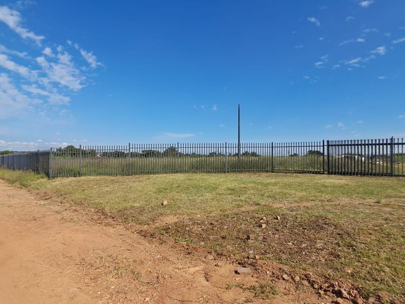 A view of a vacant commercial plot featuring perimeter steel palisade fencing and an unpaved access road.