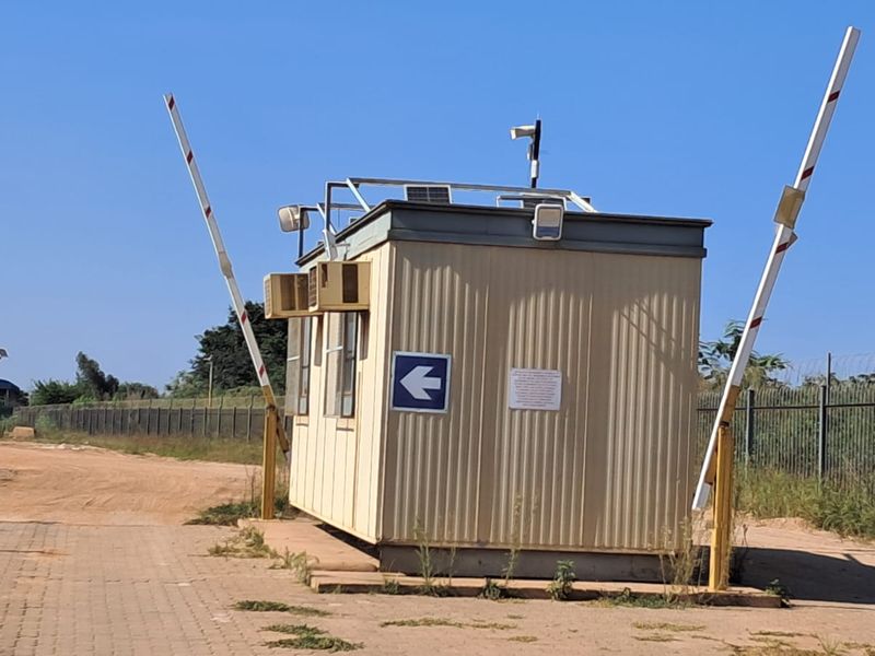 A functional security guard booth located at the property entrance, featuring integrated boom gates, security lighting, and air conditioning units.