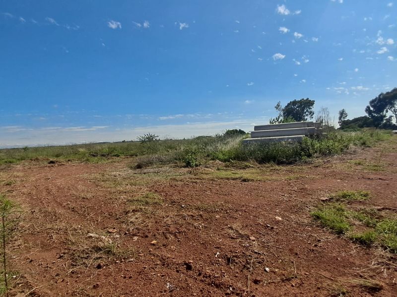 A wide-angle view of a vacant commercial land plot featuring natural terrain and some stacked concrete pipes on site.