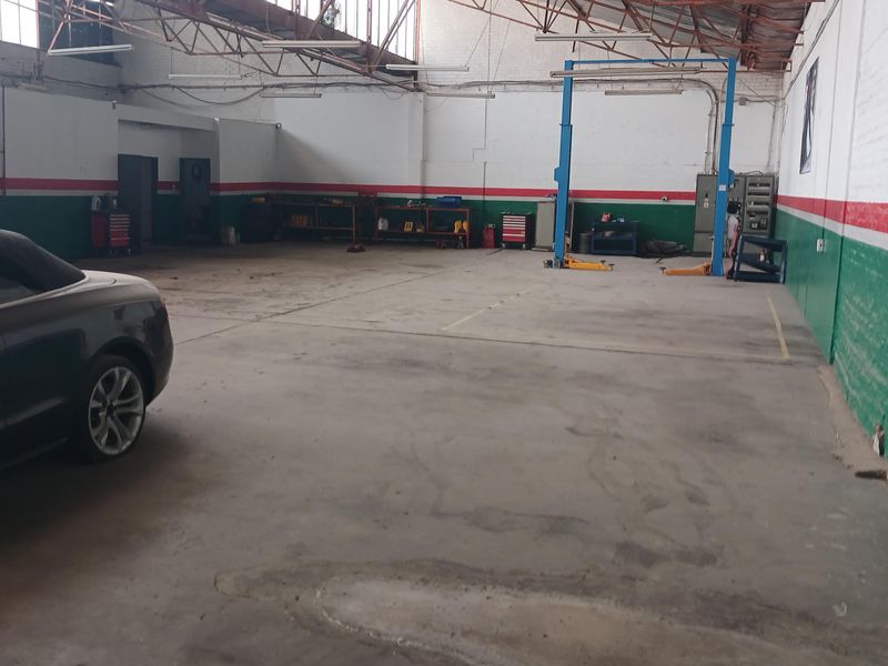 Spacious industrial workshop featuring high exposed truss ceilings, concrete flooring, and a built-in vehicle lift system.