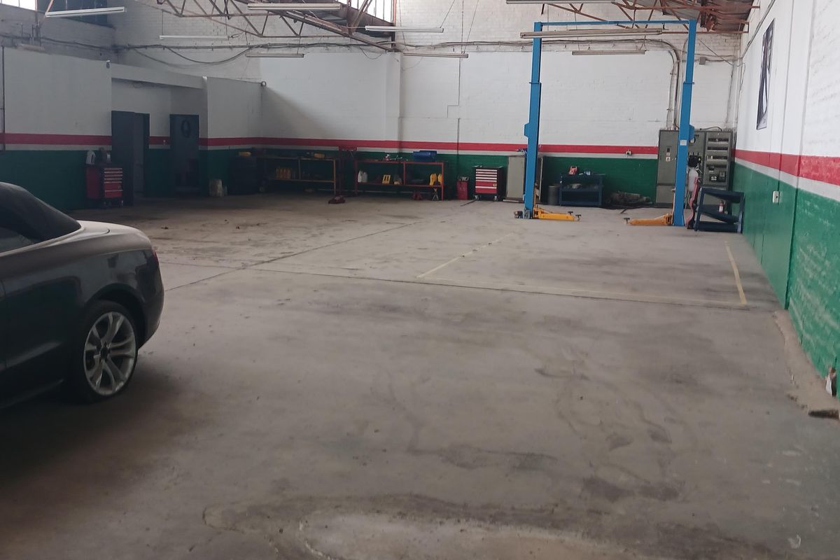Spacious industrial workshop featuring high exposed truss ceilings, concrete flooring, and a built-in vehicle lift system.
