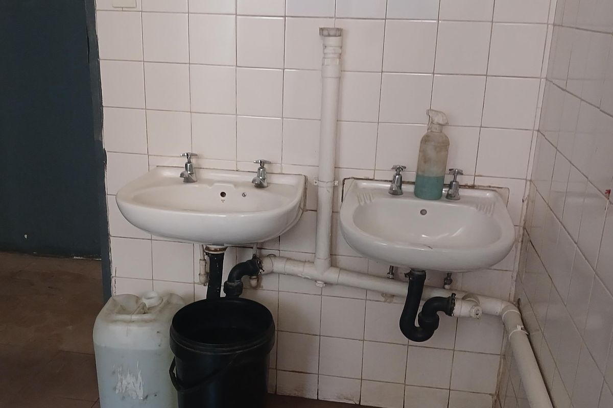 Industrial wash area featuring dual wall-mounted ceramic basins with exposed plumbing and tiled splashbacks.