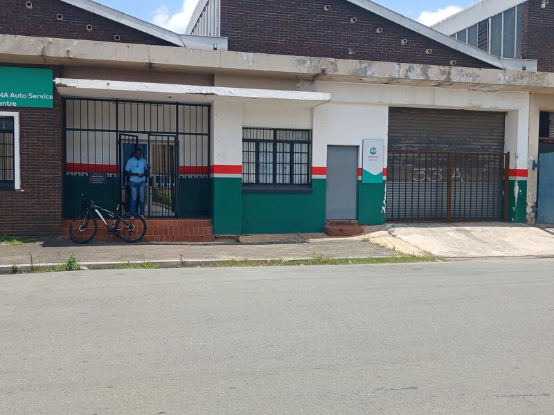 Industrial property facade featuring a roller shutter door, security gates, and brick construction, suitable for automotive or workshop use.