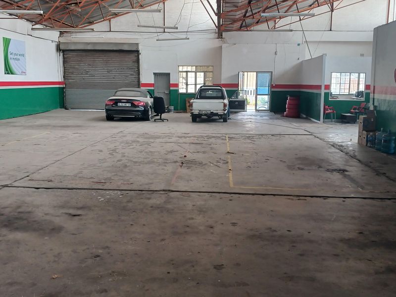 Spacious industrial warehouse featuring high exposed steel truss ceilings, concrete flooring, and a large roller shutter door for vehicle access.