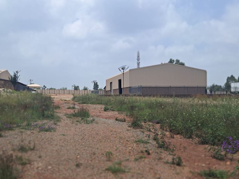 View of a commercial property site featuring industrial warehouse structures, open land, and perimeter fencing.