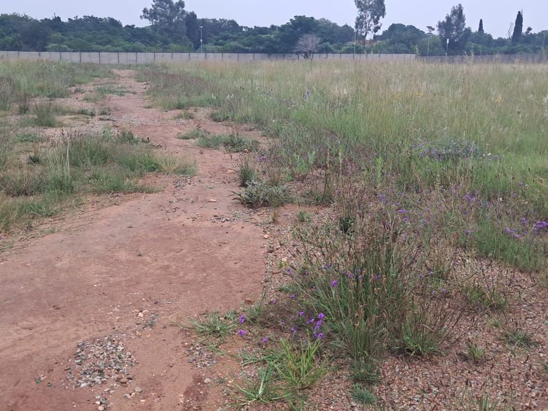 A view of the vacant commercial land, featuring an open, undeveloped plot with natural vegetation and perimeter fencing in the background.