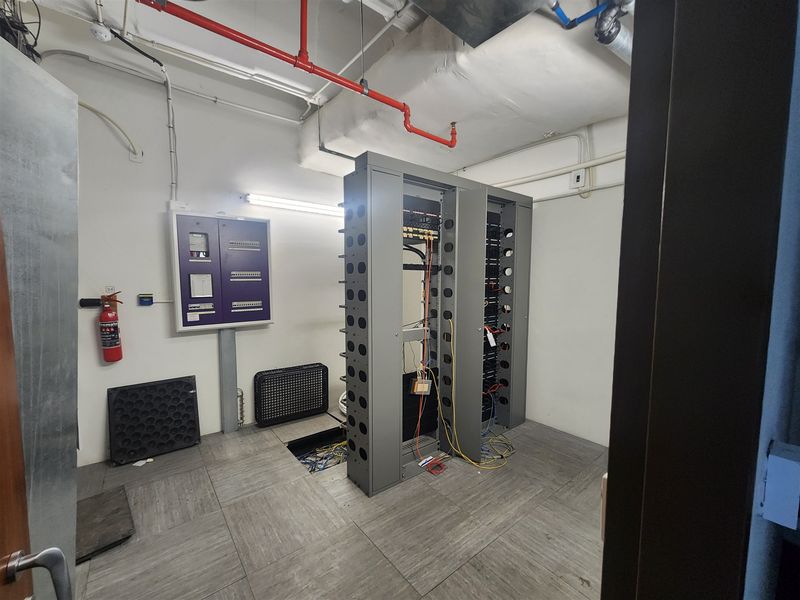 A functional server room featuring a central server rack, electrical distribution board, and exposed fire safety infrastructure with raised floor access.