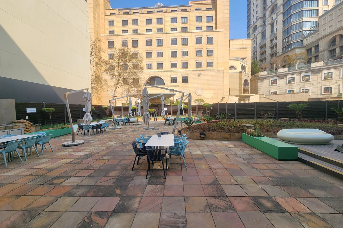 Spacious outdoor patio area featuring paved flooring, raised garden beds, and perimeter fencing, suitable for office break-out space or outdoor meetings.