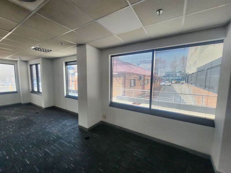 A vacant office space featuring a suspended ceiling, recessed lighting, carpet tiles, and large windows with venetian blinds providing natural light.