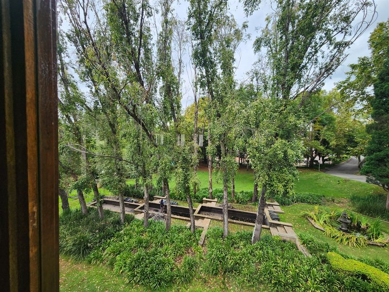 A scenic elevated view overlooking a lush, well-maintained garden featuring mature trees and a structured water feature.