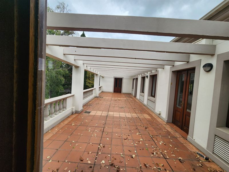 A spacious covered balcony featuring a pergola structure, terracotta tiling, and a classic balustrade, offering a versatile outdoor area for the office space.