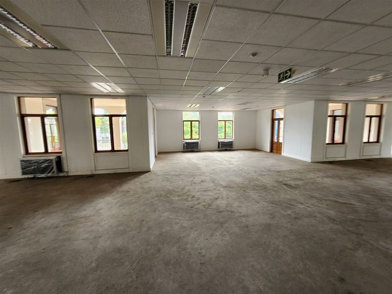 Spacious, vacant open-plan office area featuring suspended ceilings, recessed lighting, multiple windows, and wall-mounted air conditioning units.