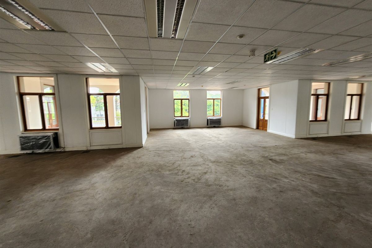 Spacious, vacant open-plan office area featuring suspended ceilings, recessed lighting, multiple windows, and wall-mounted air conditioning units.