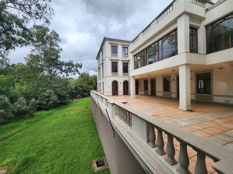 Spacious rear exterior patio featuring tiled flooring, classic balustrades, and a covered terrace area overlooking the landscaped garden and surrounding greenery.