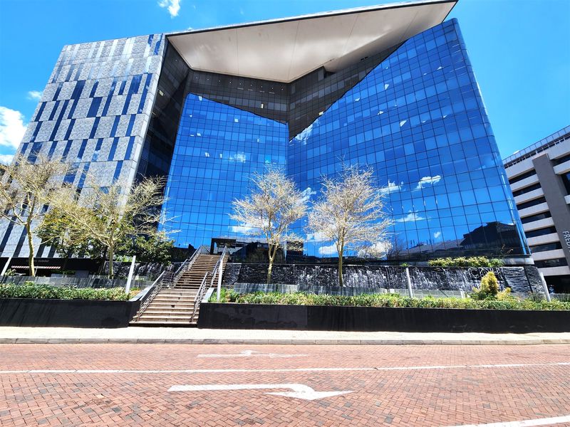 Modern commercial office building featuring a striking glass facade, integrated water feature, and stone staircase entrance from the street level.