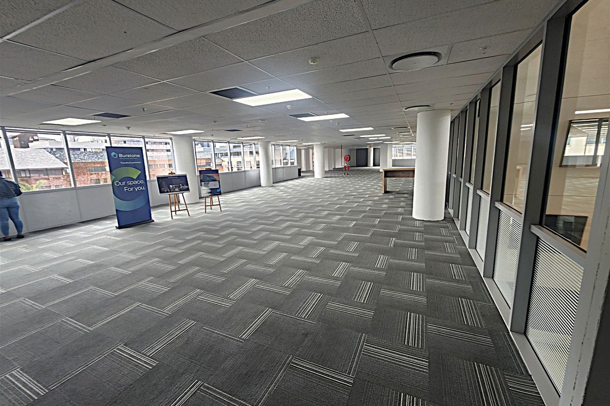 Spacious open-plan office area featuring large windows, carpeted flooring, suspended ceilings with recessed lighting, and glass partitioning for a bright, professional workspace.