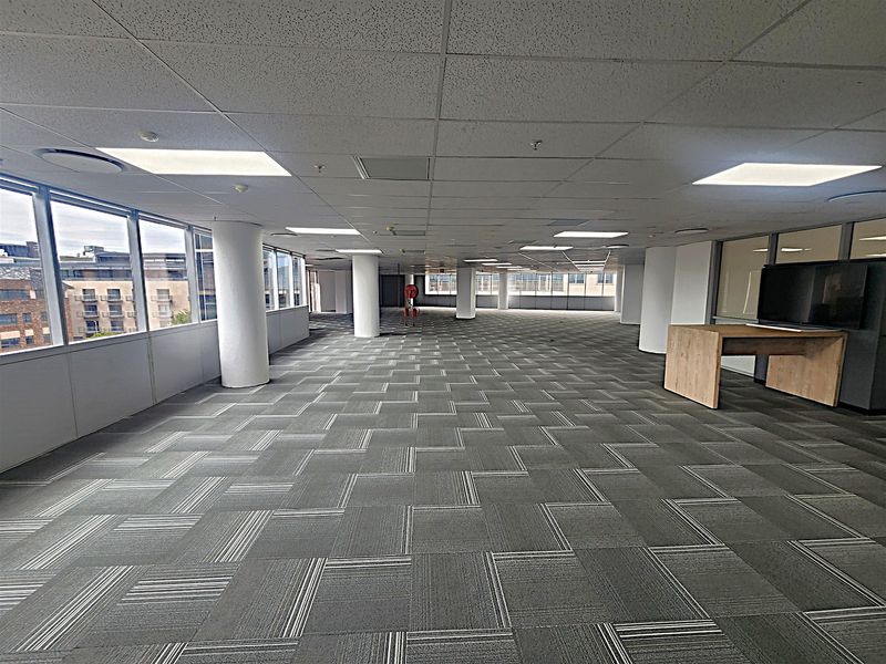 Spacious open-plan office area featuring large windows, carpet tiles, and a suspended ceiling, offering a bright and flexible workspace environment.