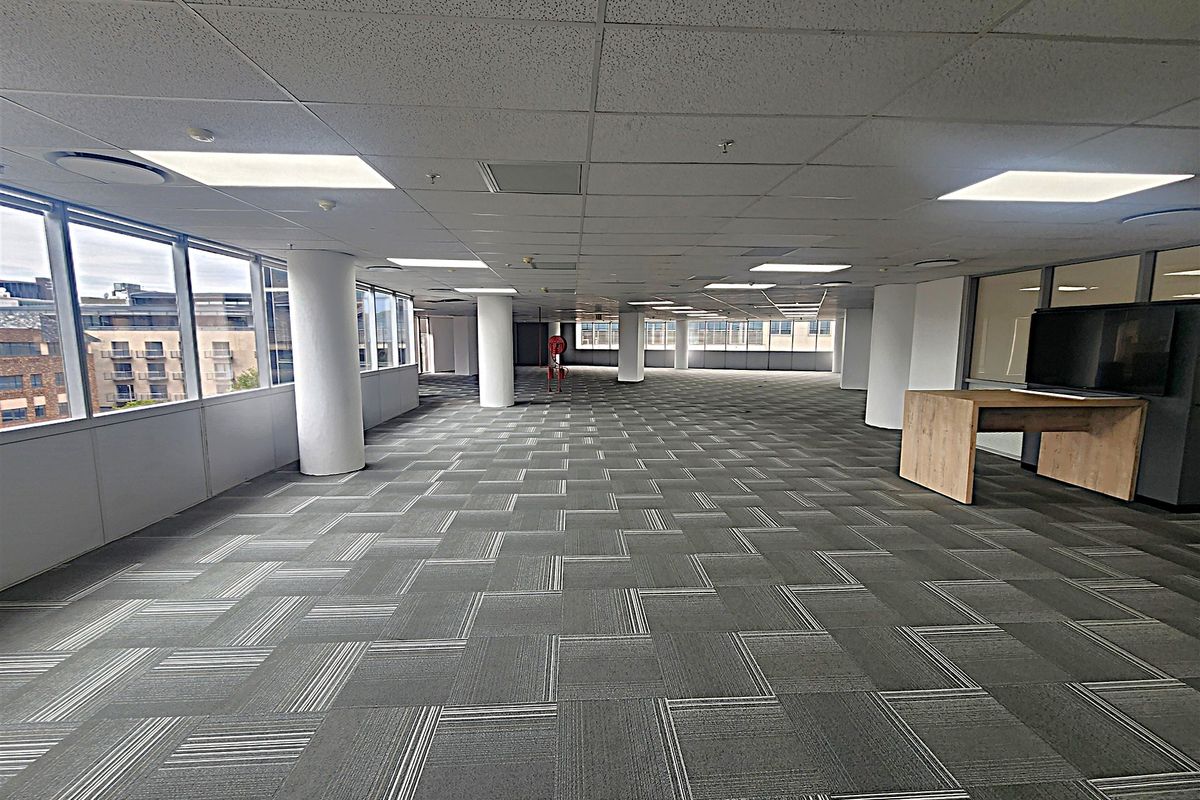 Spacious open-plan office area featuring large windows, carpet tiles, and a suspended ceiling, offering a bright and flexible workspace environment.