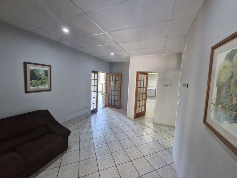 A bright commercial hallway featuring tiled flooring, suspended ceiling tiles with recessed lighting, and timber-framed glass doors providing access to adjacent office spaces.
