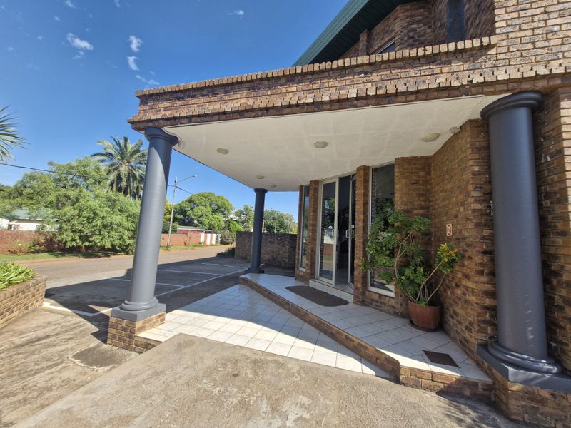 Front entrance of a commercial brick building featuring a covered porch with tiled flooring and structural columns.