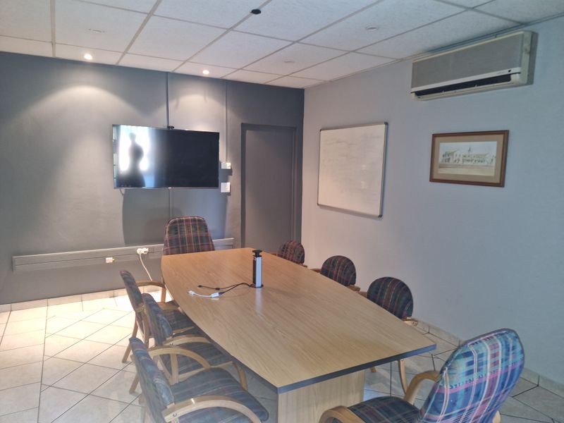 A functional commercial office or boardroom featuring tiled flooring, a suspended ceiling, wall-mounted air conditioning, and integrated electrical trunking.