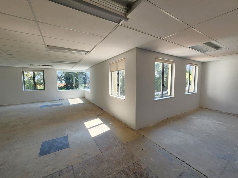 An empty, open-plan office space featuring a suspended ceiling, fluorescent lighting, and multiple windows with roller blinds, requiring new flooring installation.
