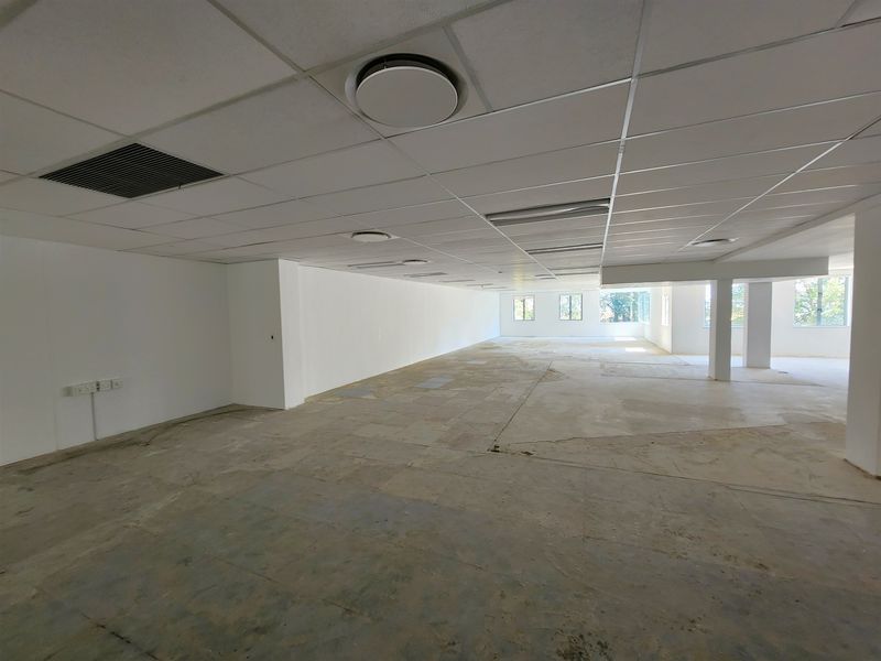 A large, open-plan office space featuring a suspended ceiling, recessed lighting, and structural columns, currently awaiting final flooring installation.