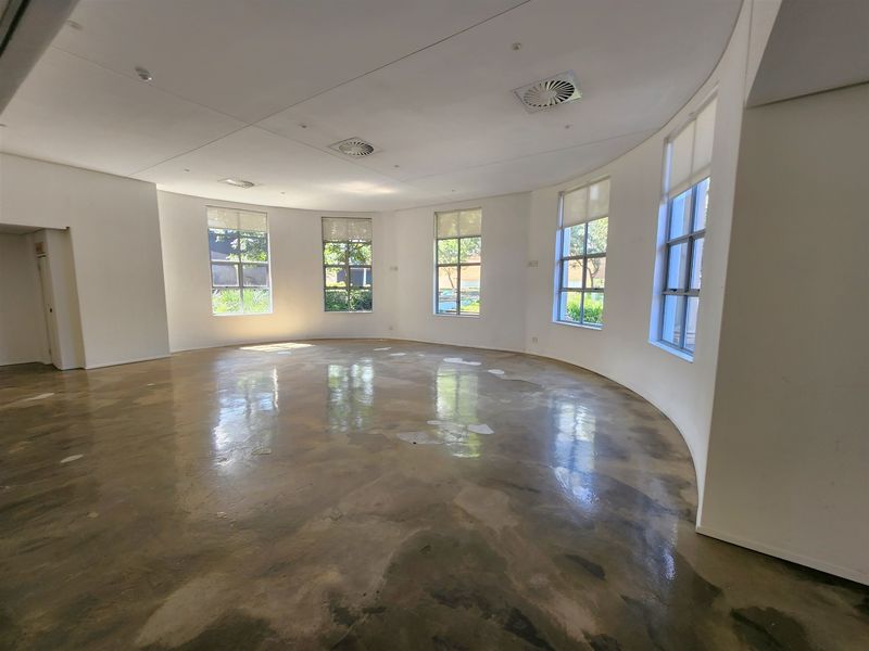 Spacious, empty circular office area featuring polished concrete floors, large windows providing natural light, and integrated ceiling air conditioning vents.