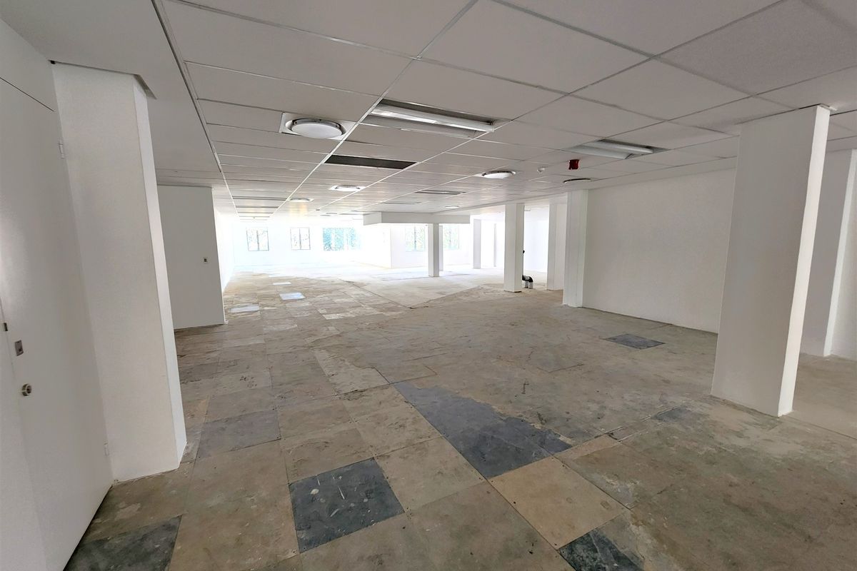 An expansive, open-plan office space featuring a suspended ceiling, recessed lighting, and structural columns, currently awaiting new flooring and final finishes.