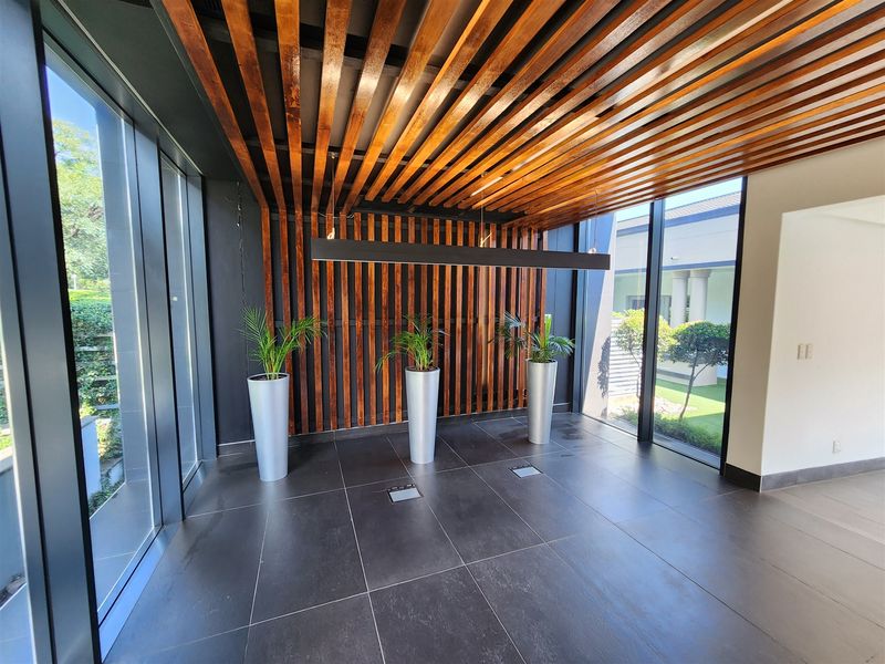 Modern office entrance featuring a striking timber slat ceiling and wall design, large format floor tiles, and expansive floor-to-ceiling glass windows.