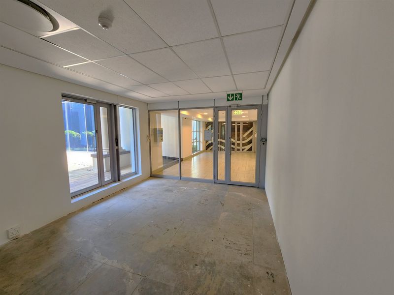 An empty, open-plan office space featuring a suspended ceiling, glass partition doors, and unfinished concrete flooring, ready for custom fit-out.