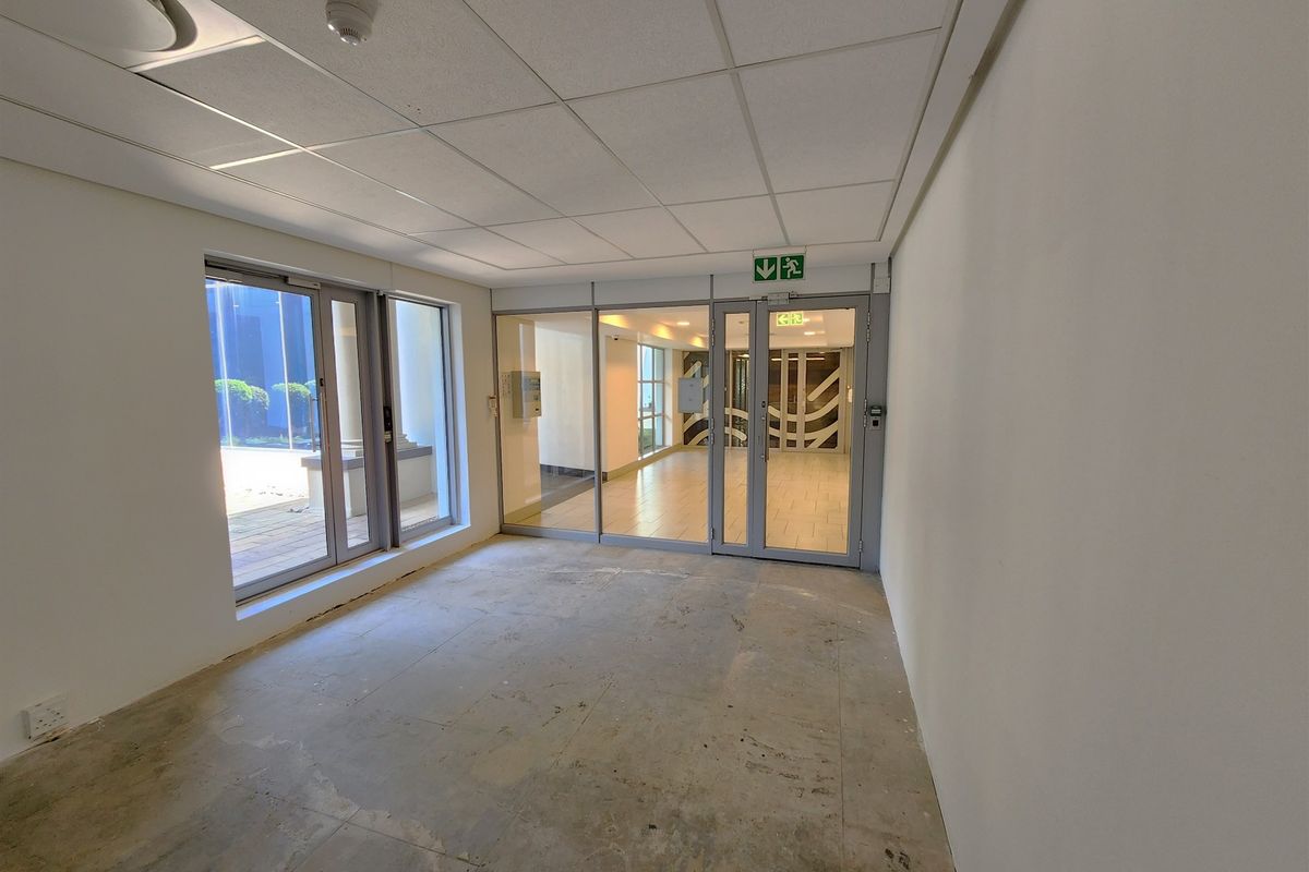 An empty, open-plan office space featuring a suspended ceiling, glass partition doors, and unfinished concrete flooring, ready for custom fit-out.