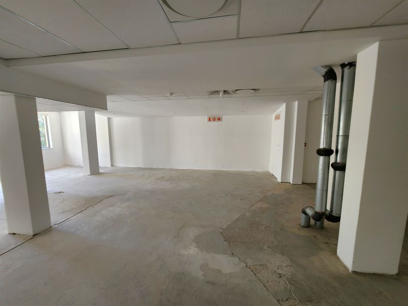 An open-plan office space featuring exposed ventilation ducting, structural columns, and a suspended ceiling, currently in a shell condition with concrete flooring.