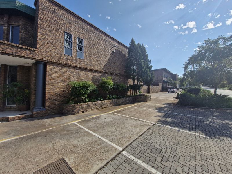 Exterior view of a commercial property featuring a face brick facade, paved parking bays, and established garden planter boxes.