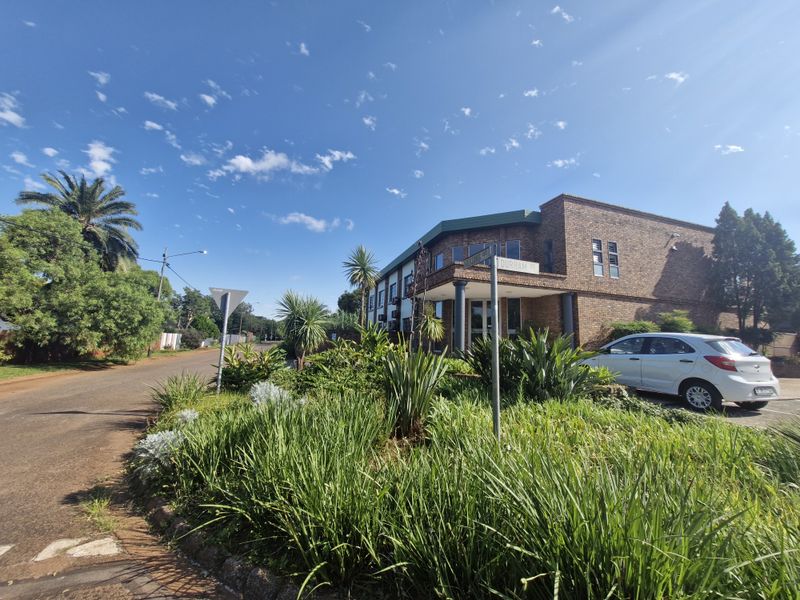 A street-level view of a commercial brick building featuring a landscaped garden, paved driveway, and a covered entrance area.