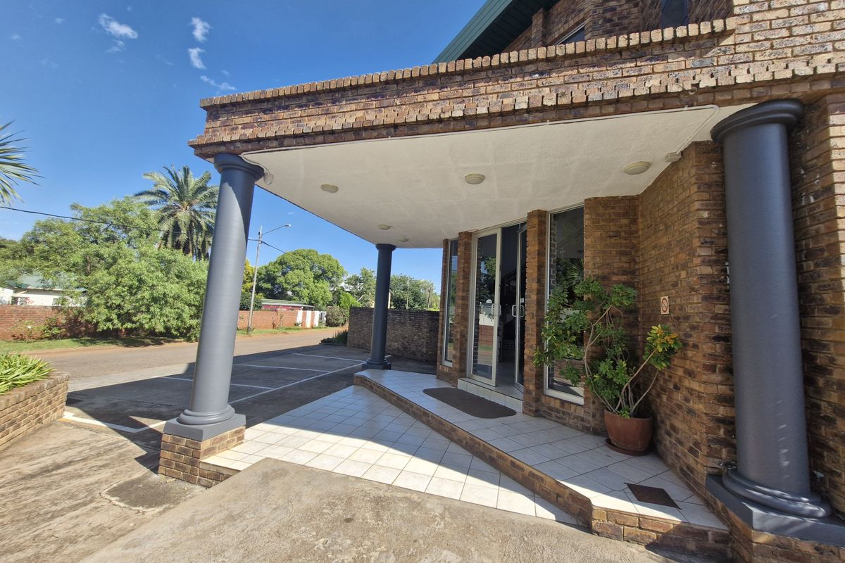 Front entrance of a commercial brick building featuring a covered porch with tiled flooring and structural columns.