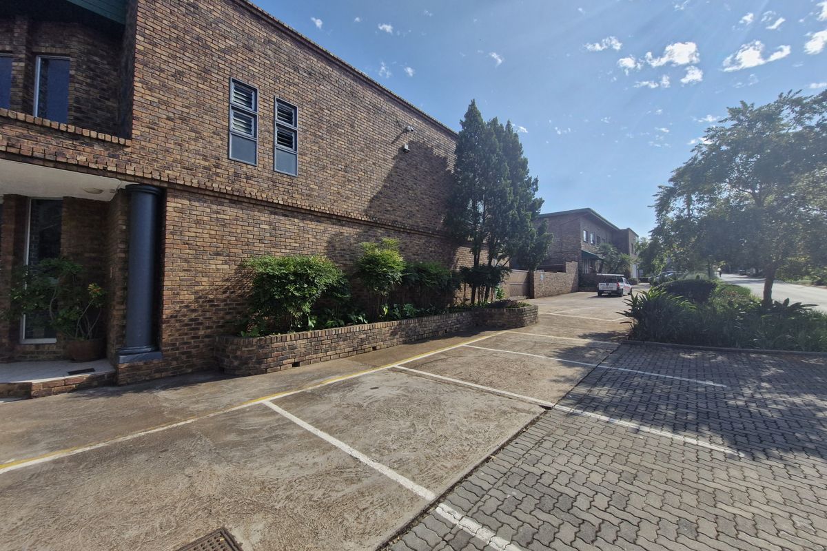 Exterior view of a commercial property featuring a face brick facade, paved parking bays, and established garden planter boxes.