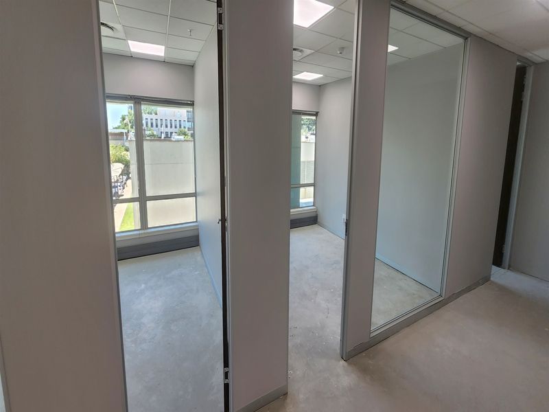 Two vacant office suites featuring glass partition walls, suspended ceilings with recessed lighting, and large windows providing natural light.