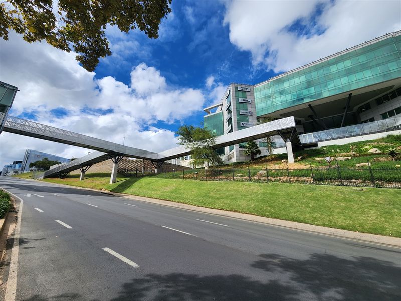 Modern office building exterior featuring a glass facade and a prominent pedestrian skybridge connecting to the main structure.