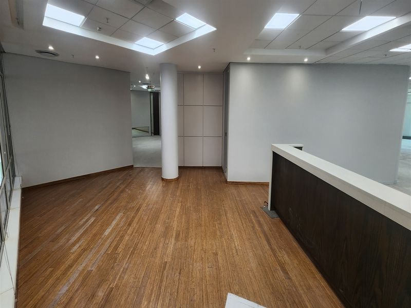 An empty office space featuring bamboo flooring, a built-in reception counter, recessed ceiling lighting, and neutral wall finishes.