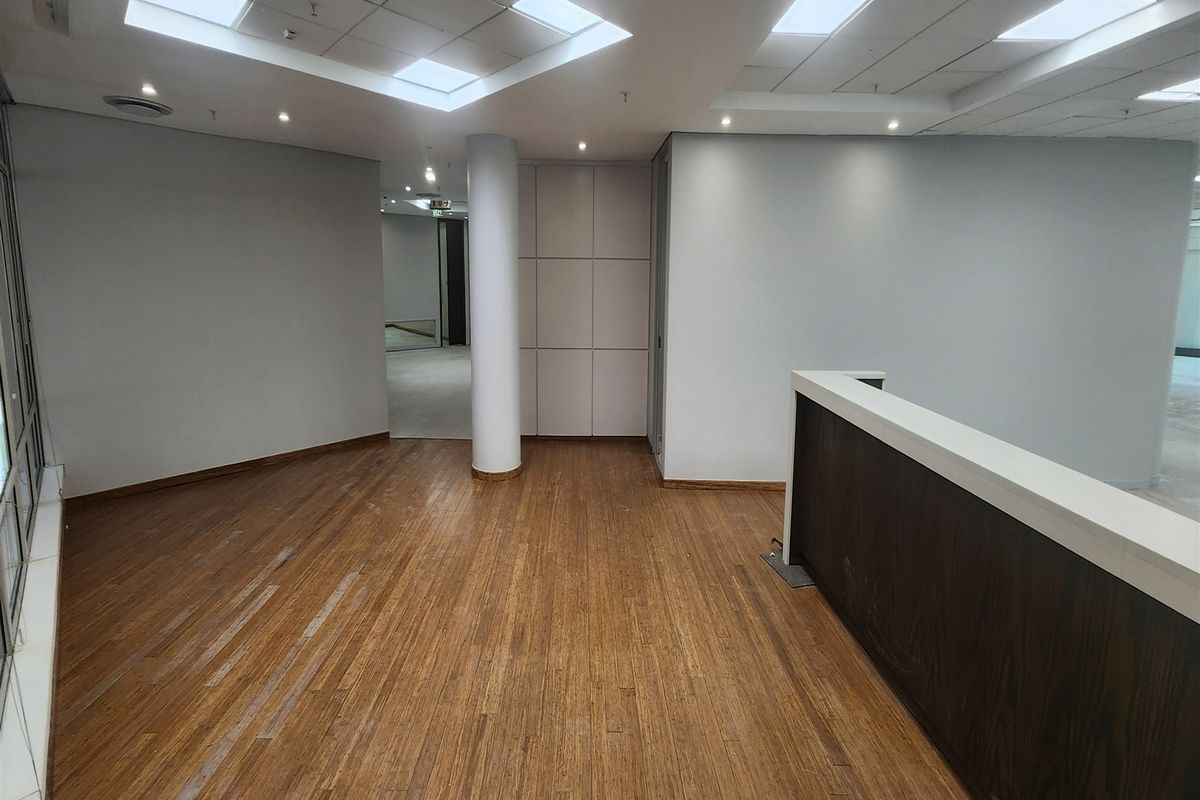 An empty office space featuring bamboo flooring, a built-in reception counter, recessed ceiling lighting, and neutral wall finishes.