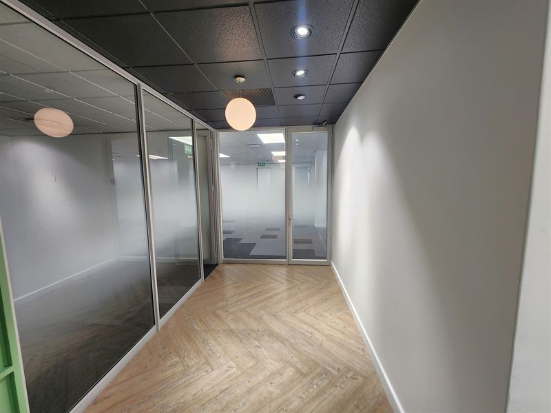 Modern office space featuring glass partitions, herringbone vinyl flooring, and a contemporary black suspended ceiling with recessed lighting.