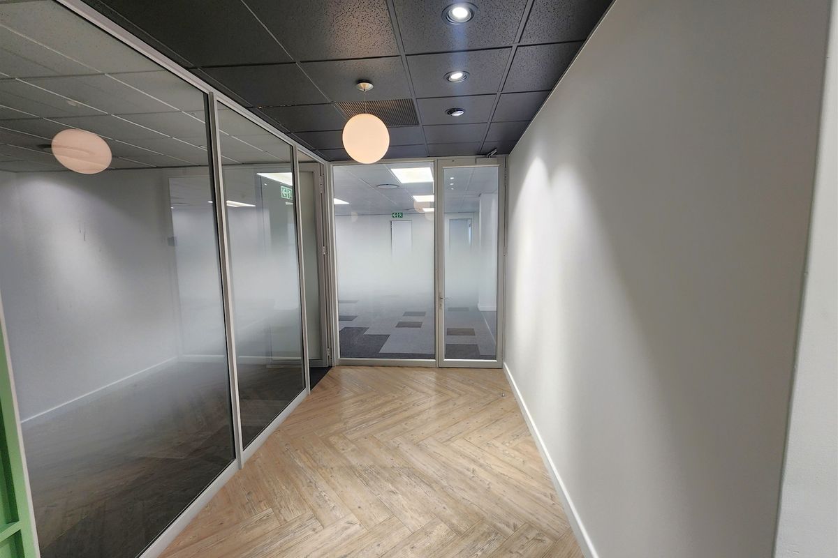 Modern office space featuring glass partitions, herringbone vinyl flooring, and a contemporary black suspended ceiling with recessed lighting.