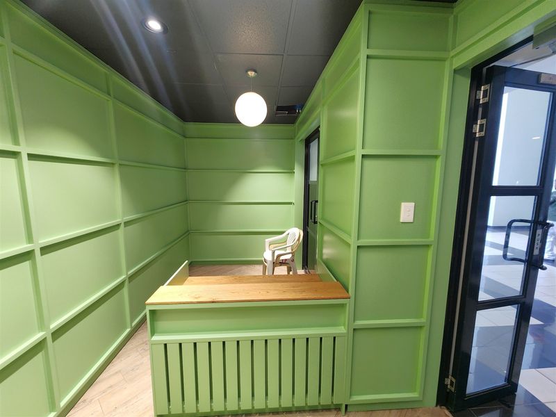 A compact office space featuring vibrant green wainscoting, a built-in reception desk, and modern lighting fixtures.
